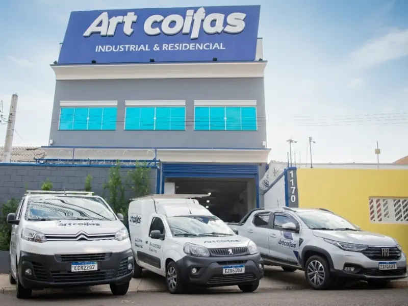 Fachada da fábrica Art Coifas com veículos utilitários estacionados e identificação visual da empresa.