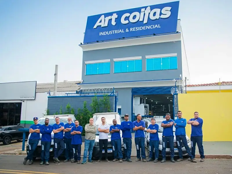 Equipe de colaboradores da Art Coifas reunida em frente à sede da fábrica e veículos.