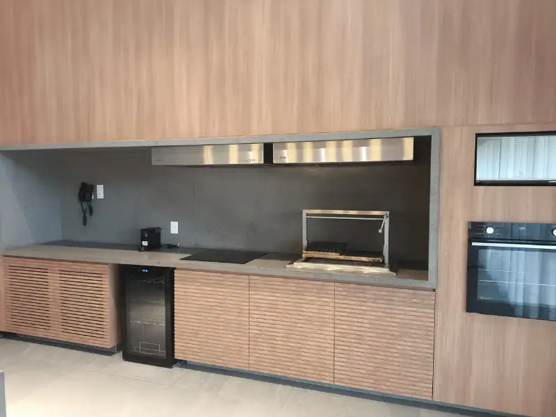 Coifa de parede em inox instalada sobre churrasqueira em área gourmet com ripas amadeiradas.